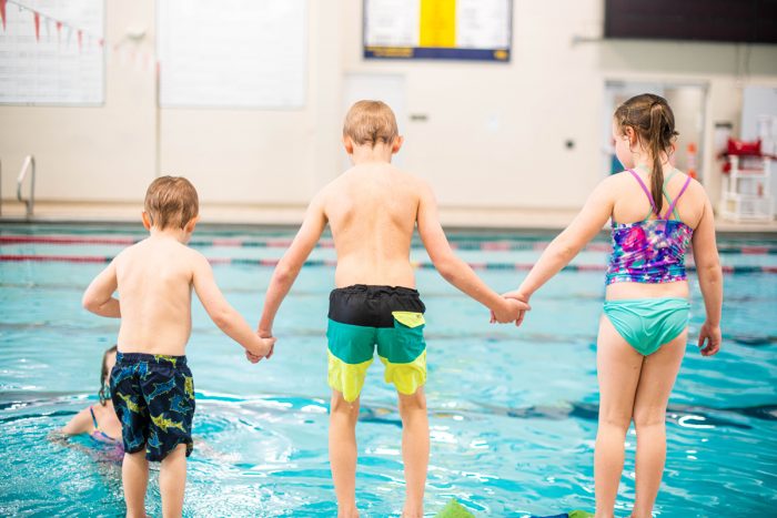 three kids holding hands on side of pool
